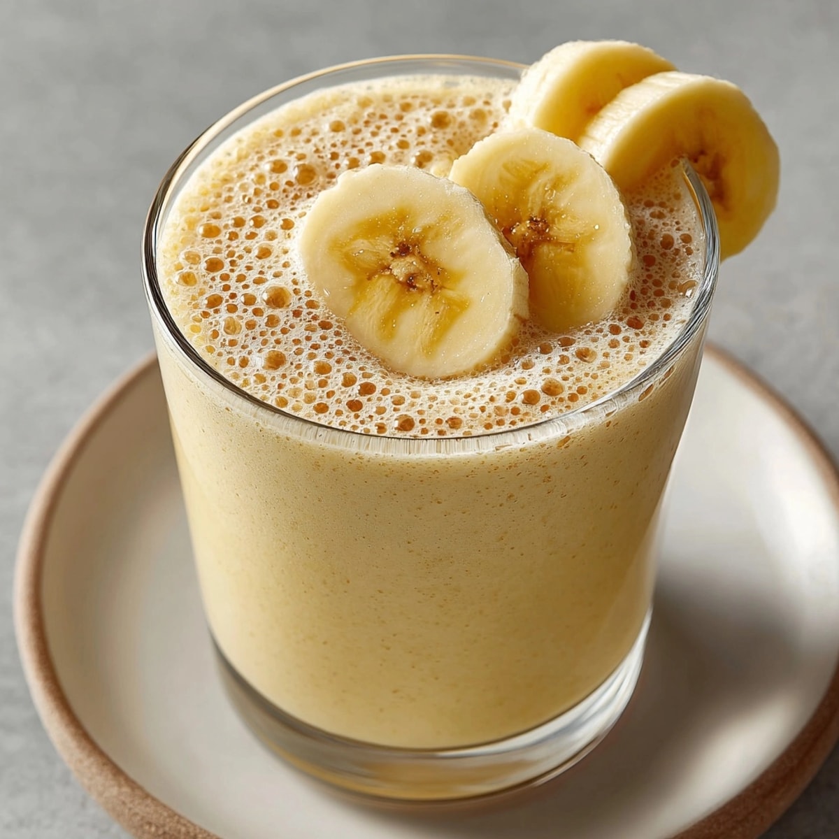 Healthy Banana Smoothie: Swirled, light yellow drink spilling from a glass, ice visible.