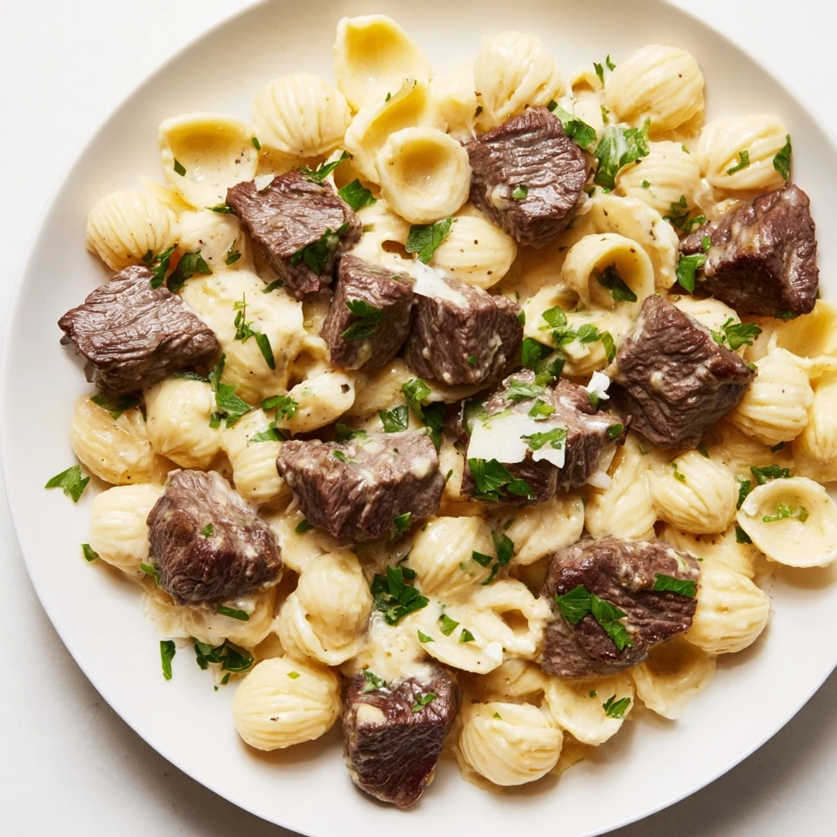 Garlic butter steak bites glistening on a bed of cheesy pasta shells; savory and delicious.