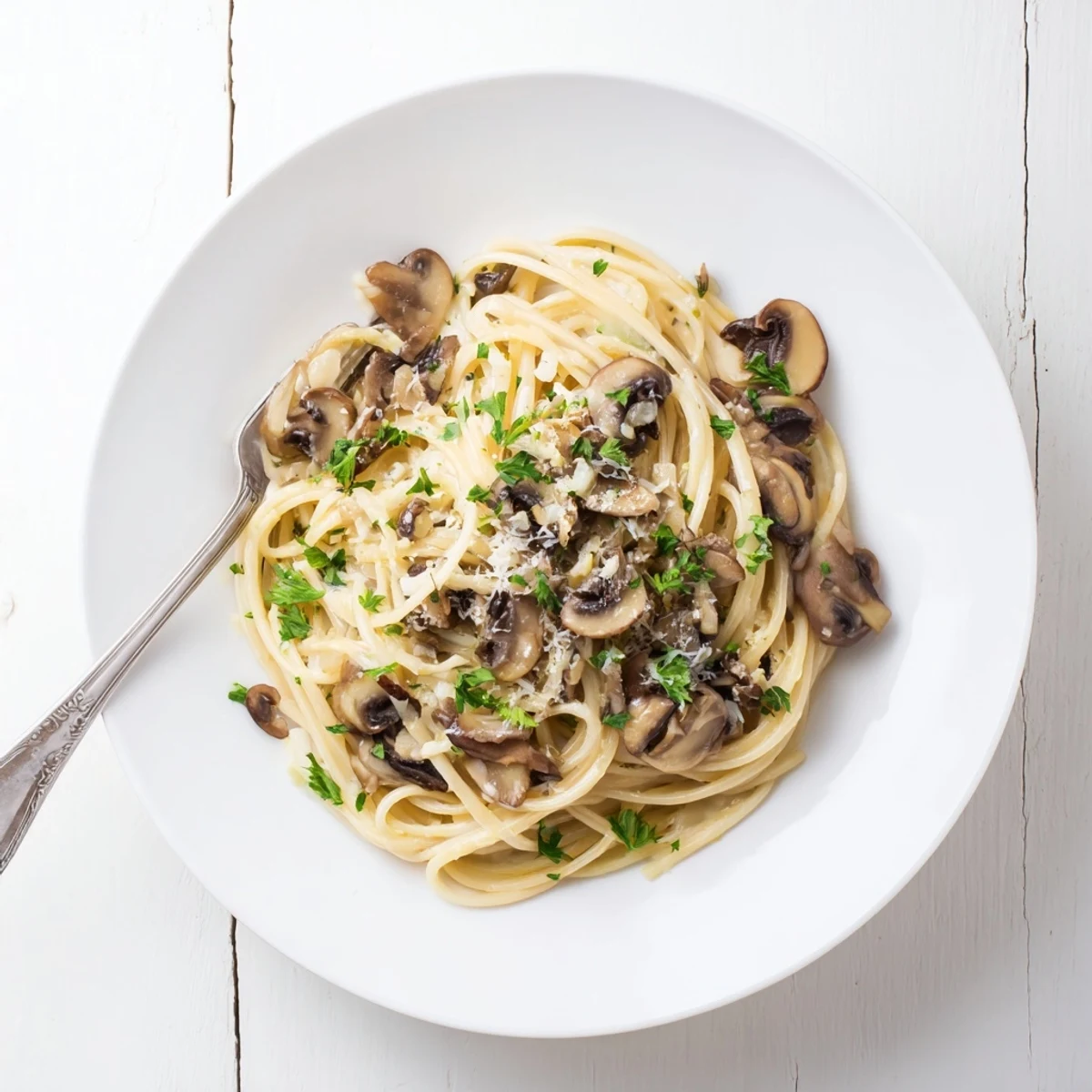 A bowl of creamy mushroom linguine topped with shaved Parmesan and fresh parsley, ready to serve.