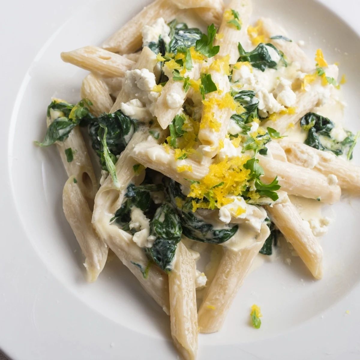 A close-up of Creamy Feta Spinach Pasta in a skillet, featuring wilted greens and crumbled cheese melting into a glossy sauce.