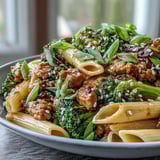 A close-up shows a fork lifting a saucy bite of Sweet & Spicy Turkey Broccoli Pasta, garnished with green onions and sesame seeds.