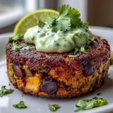 A close-up of a toasted burger bun filled with a hearty sweet potato black bean patty, drizzled with zesty avocado lime sauce.