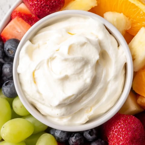 A central bowl of cold, fluffy cream cheese fruit dip, served alongside juicy strawberries.