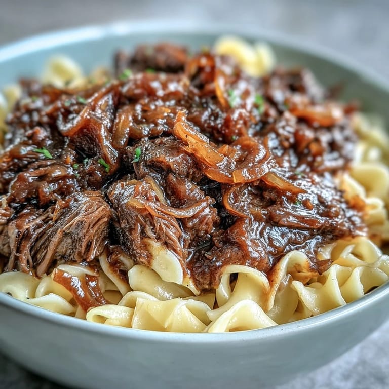 Slow-cooked Crockpot French Onion Pot Roast Pasta topped with melted Gruyère and fresh parsley on a rustic plate.