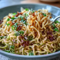A steaming bowl of viral garlic butter ramen, glistening with savory sauce and topped with soft-boiled egg and green onions.